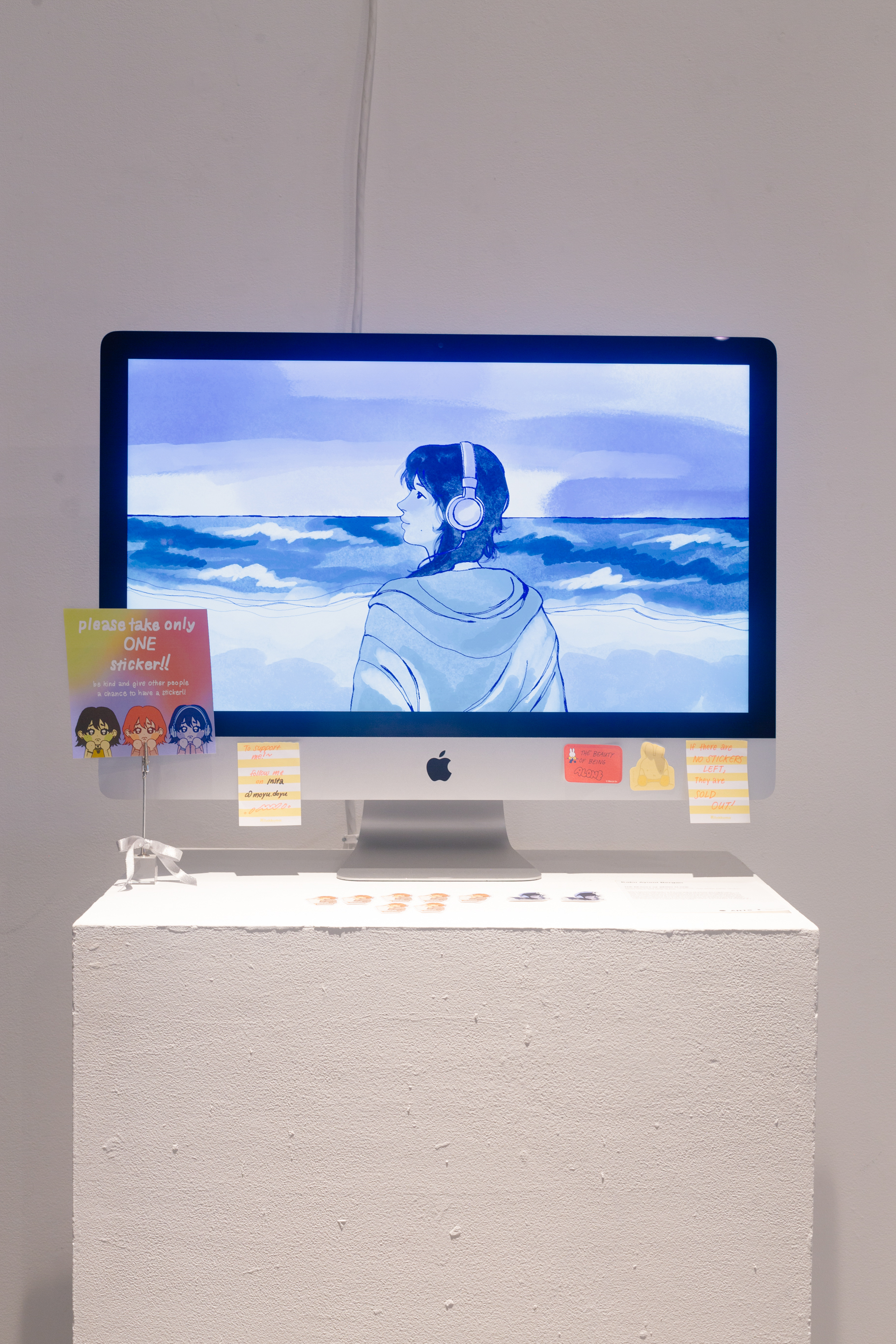 A computer monitor on a tall podium with illustrations displayed on it, against a plain white wall